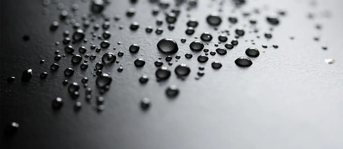 Eine schwarze Metalloberfläche auf der mehrere Wassertropfen angesammelt sind.