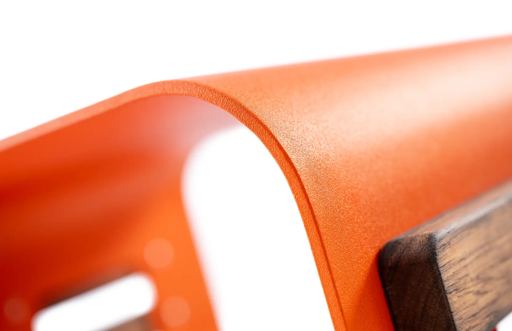 Detailaufnahme eines geschwungenen Design Liege Sessels, orangefarbene Metalloberfläche mit einer schrägen Holzleiste